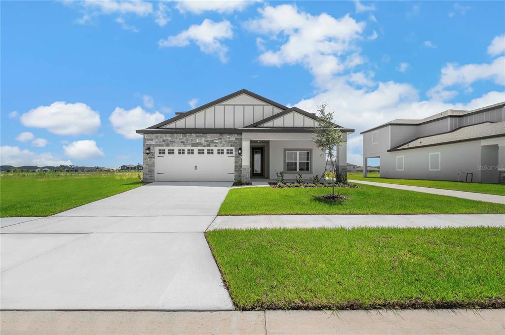 A single-story house with a stone facade, white garage door, and a concrete driveway — 3368 CHINOTTO DRIVE, LAKE ALFRED, FL