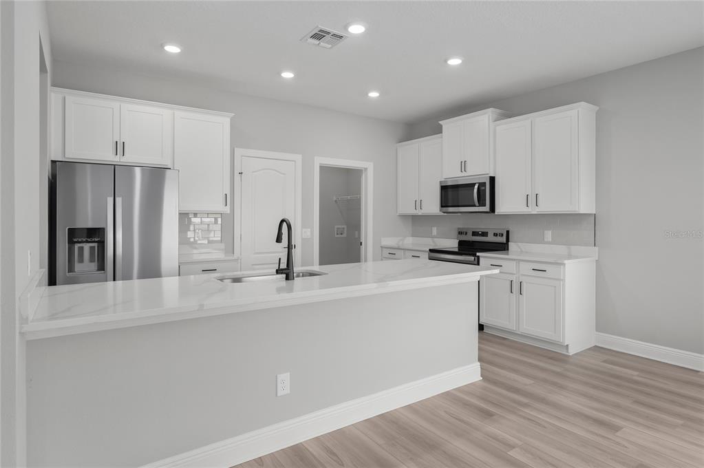 A modern kitchen features white cabinets, stainless steel appliances, and a white quartz island countertop — 3368 CHINOTTO DRIVE, LAKE ALFRED, FL