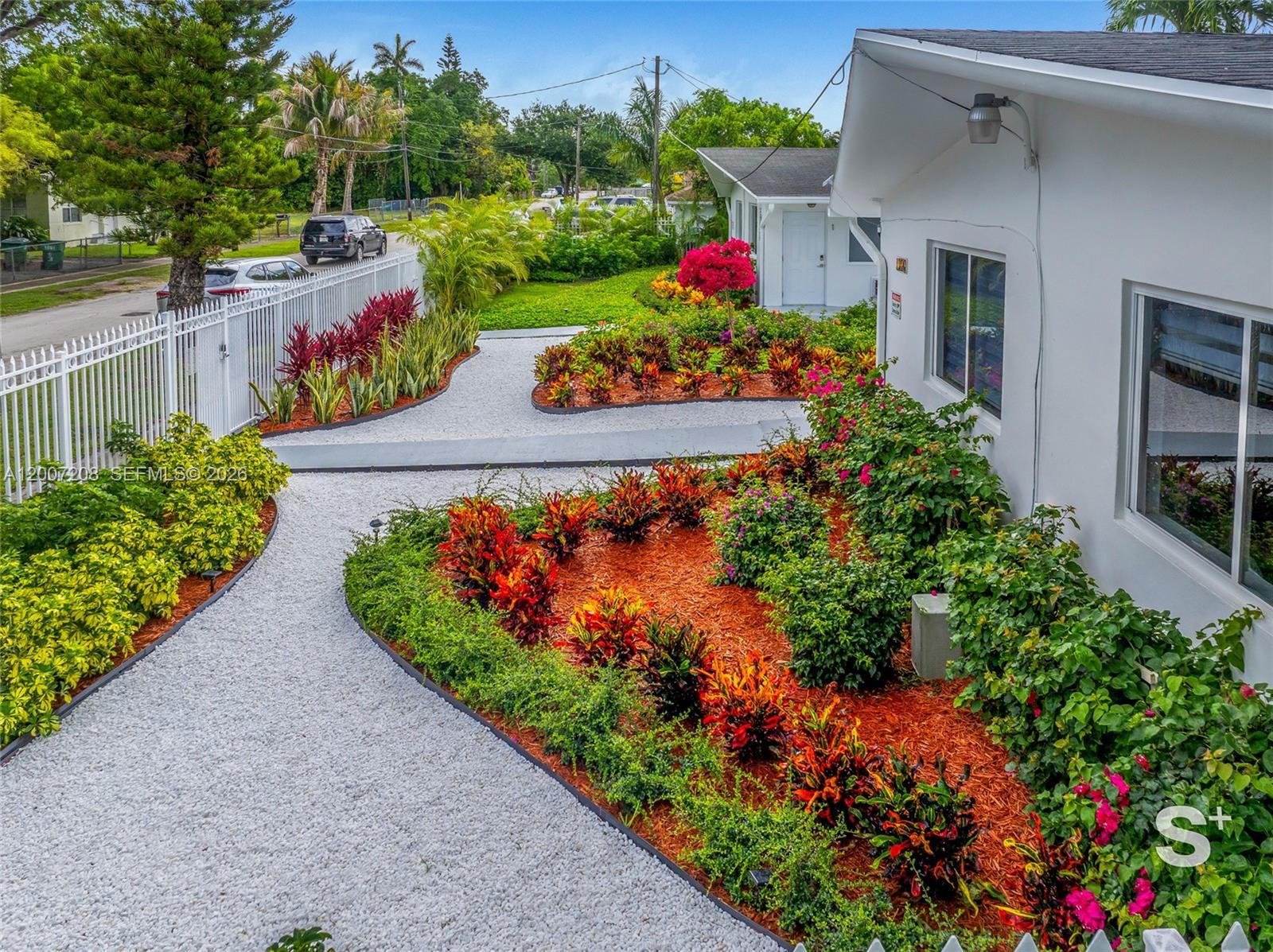 An exterior view of a white house with landscaped gardens, gravel paths, and a fence — 1300 NE 110th St, Miami FL 33161, MIAMI, FL
