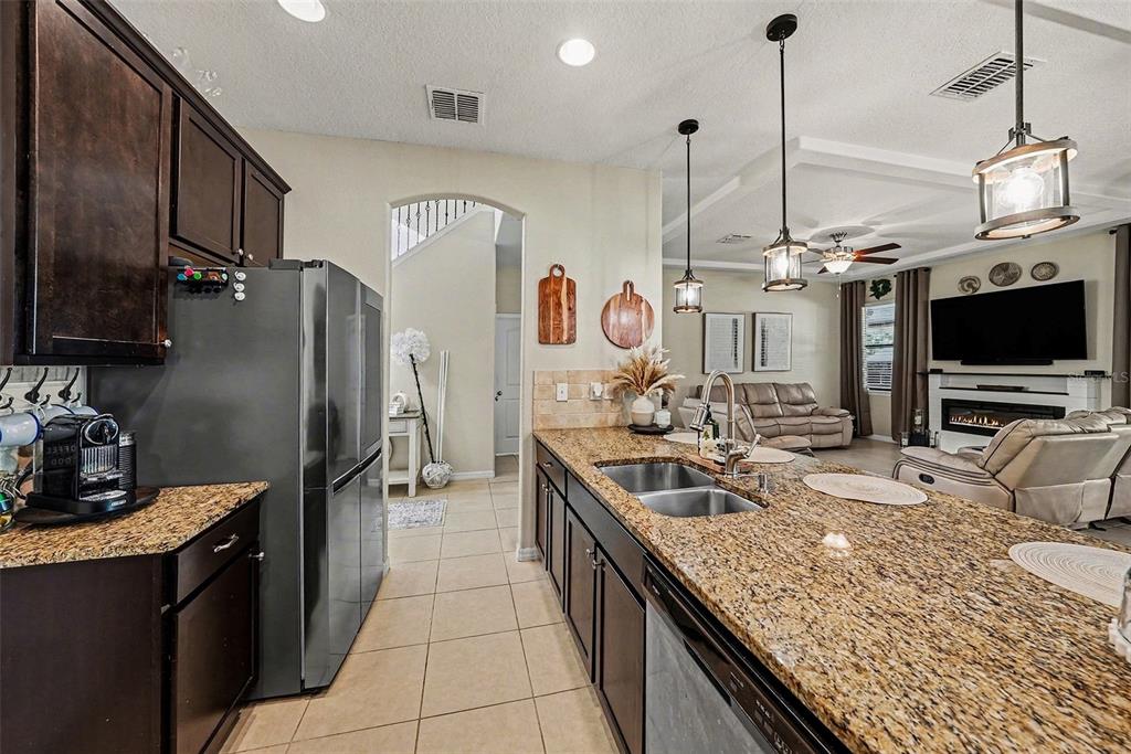 A kitchen with dark cabinets and granite countertops opens into a living room area — 12530 BALLENTRAE FOREST DRIVE, RIVERVIEW, FL