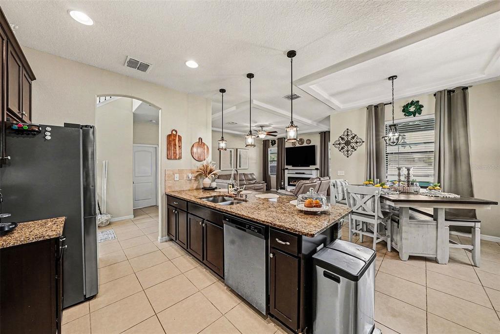 A kitchen with dark cabinets, granite countertops, and an island opens to a dining area — 12530 BALLENTRAE FOREST DRIVE, RIVERVIEW, FL