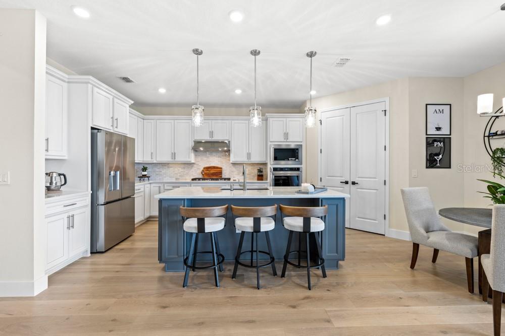A modern kitchen features white cabinetry, a blue island with bar seating, and stainless appliances — 5148 FOOTHILLS PRESERVE LOOP, MOUNT DORA, FL