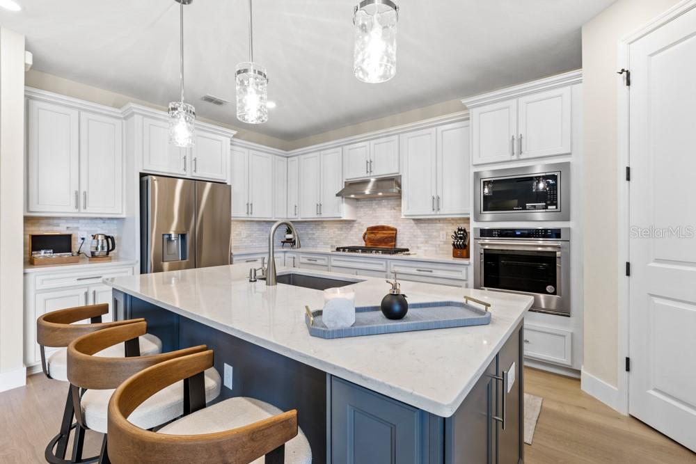 A modern kitchen features white cabinetry, a dark blue island with seating, and stainless appliances — 5148 FOOTHILLS PRESERVE LOOP, MOUNT DORA, FL