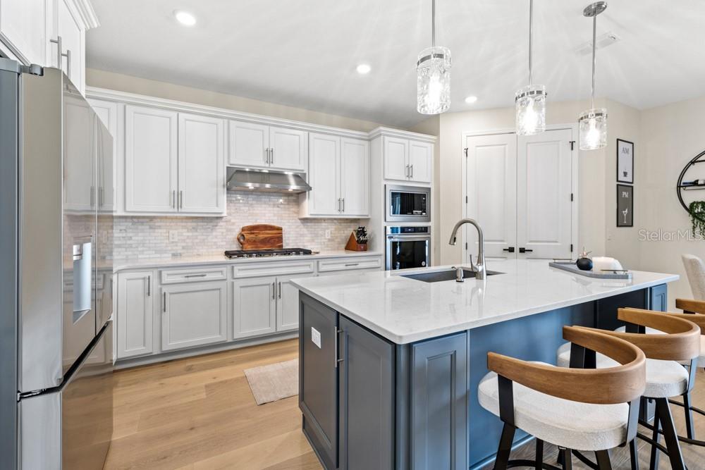 A modern kitchen features white cabinetry, a dark blue island, and stainless steel appliances — 5148 FOOTHILLS PRESERVE LOOP, MOUNT DORA, FL