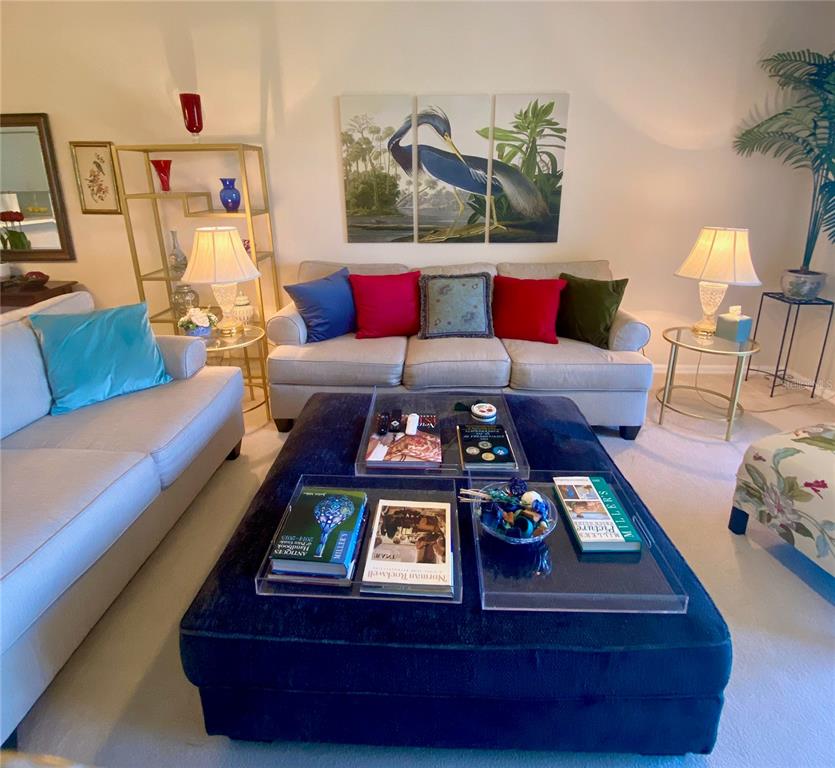 A living room features a large blue ottoman, two beige sofas, and a gold shelving unit — 9590 HIGH GATE DRIVE UNIT 1915, SARASOTA, FL