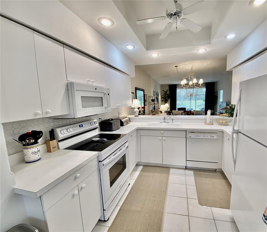 A white kitchen features white cabinetry, white appliances, and a tiled floor — 9590 HIGH GATE DRIVE UNIT 1915, SARASOTA, FL
