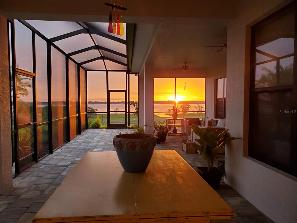 A screened-in patio with a table and potted plants overlooks a lake at sunset — 262 AMARYLLIS WAY, LAKE ALFRED, FL