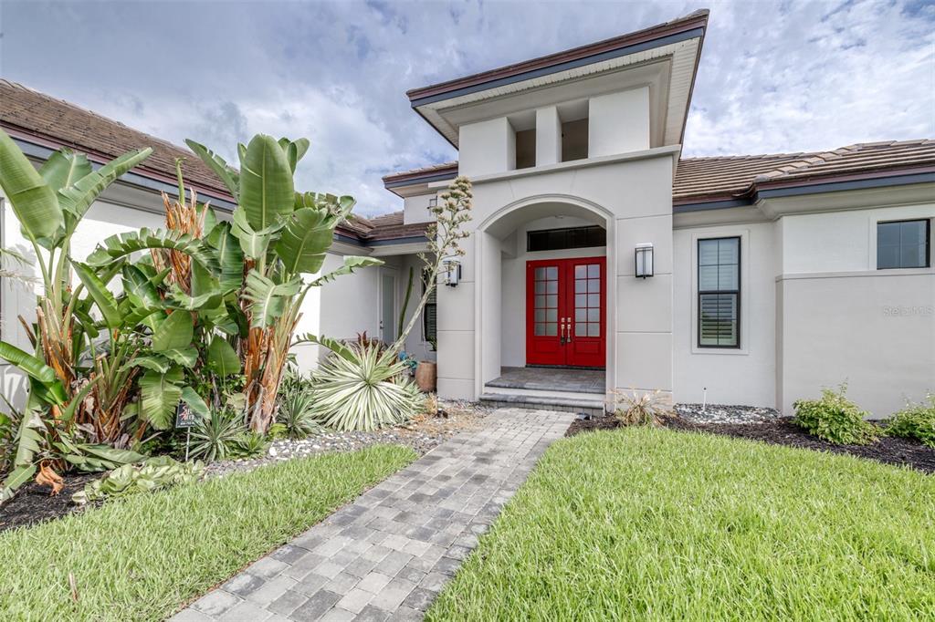 A paved walkway leads to the red double front doors of a modern stucco house — 262 AMARYLLIS WAY, LAKE ALFRED, FL