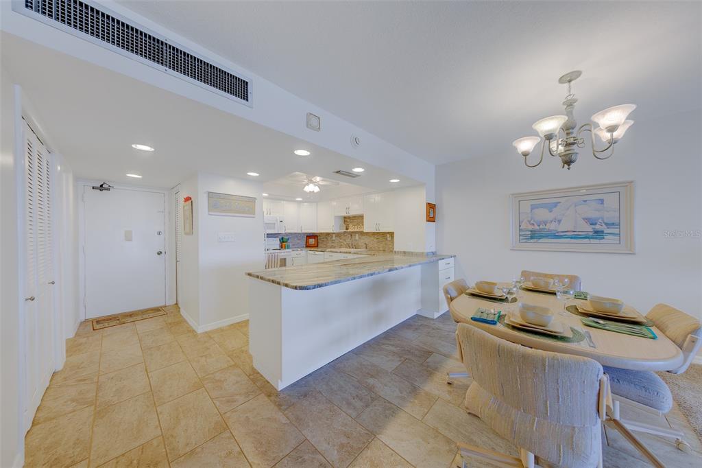 An open-concept kitchen with a breakfast bar overlooks a dining area with a chandelier — 17920 GULF BOULEVARD UNIT 1808, REDINGTON SHORES, FL