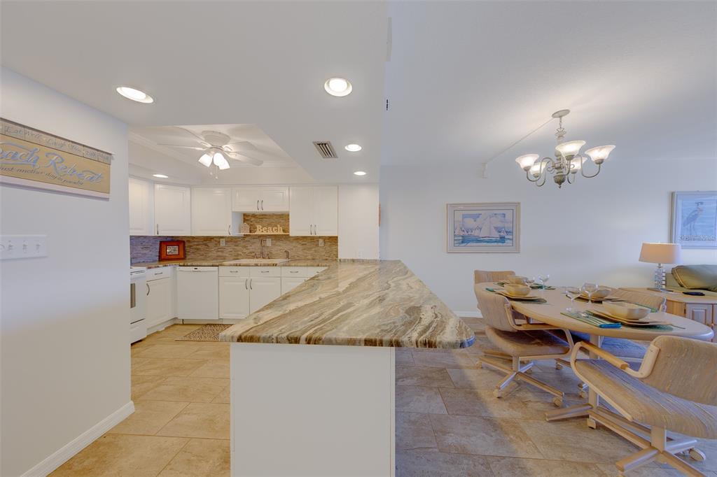 A kitchen with white cabinets and a stone countertop opens to a dining area — 17920 GULF BOULEVARD UNIT 1808, REDINGTON SHORES, FL