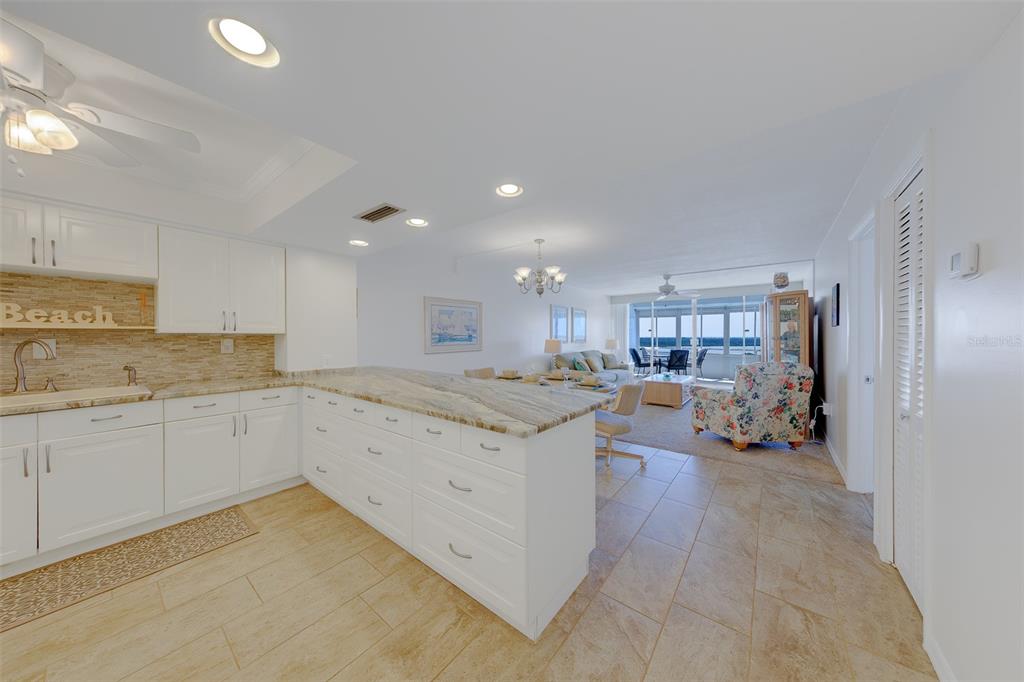 A kitchen with white cabinets and a stone island overlooks a living area with views — 17920 GULF BOULEVARD UNIT 1808, REDINGTON SHORES, FL