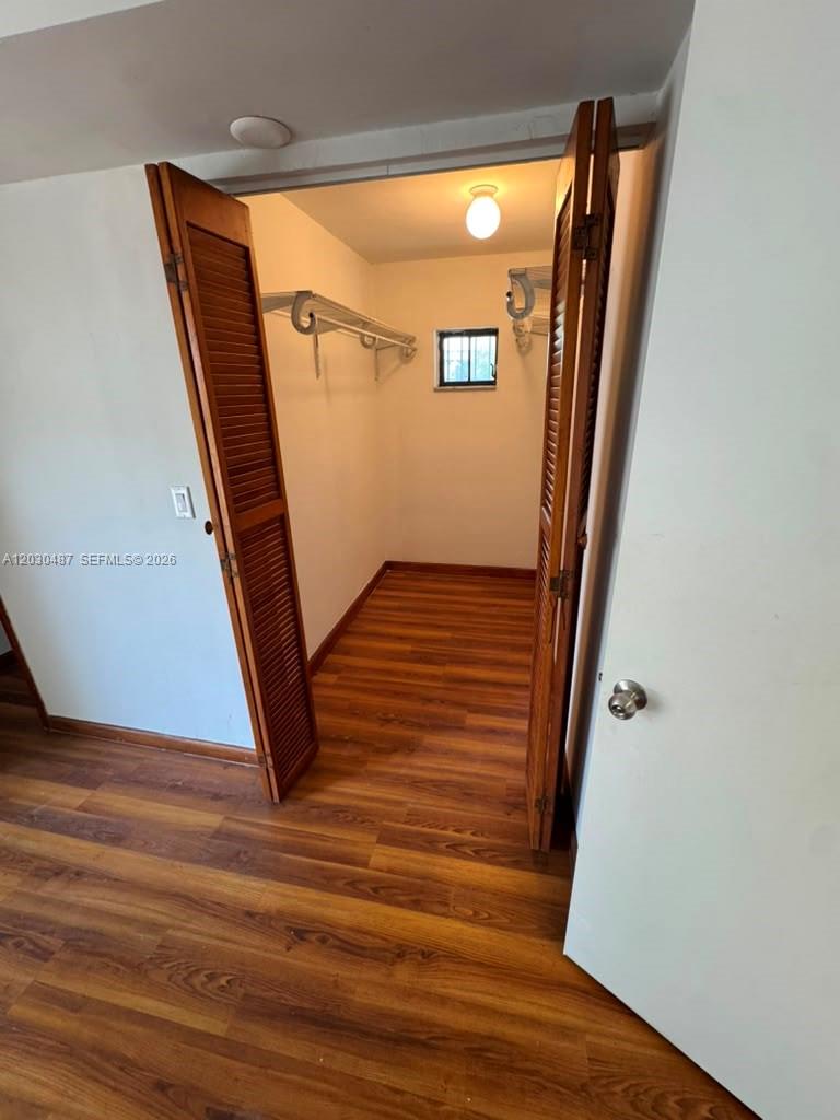 This walk-in closet features wood-look flooring, louvered doors, a shelf with a hanging rod, and a small window — 2107 Secoffee St # 3, Miami FL 33133, MIAMI, FL