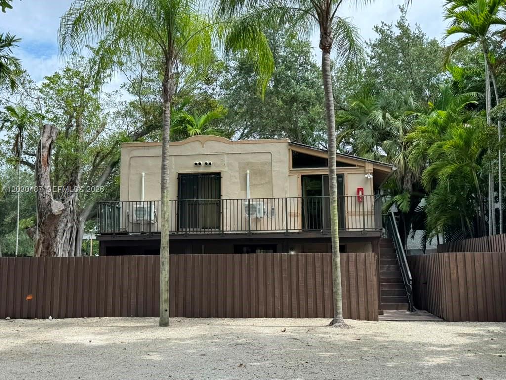 An elevated house with a balcony, metal railing, and exterior stairs behind a wooden fence — 2107 Secoffee St # 3, Miami FL 33133, MIAMI, FL