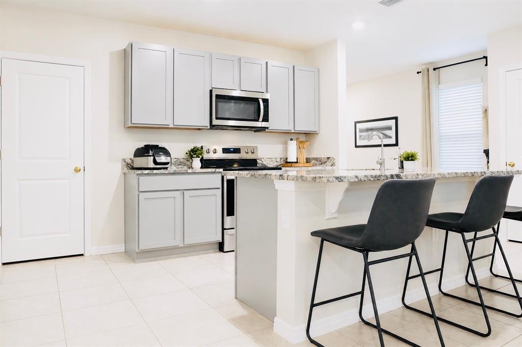 A kitchen features light gray cabinets, granite countertops, stainless steel appliances, and a breakfast bar — 17015 OVAL RUM DRIVE, WIMAUMA, FL
