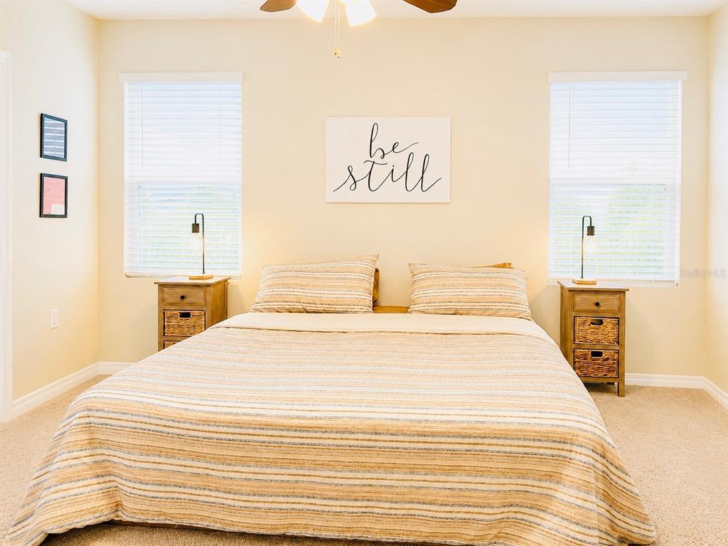 A bedroom features a bed with striped bedding, two wooden nightstands, and a wall sign — 17015 OVAL RUM DRIVE, WIMAUMA, FL