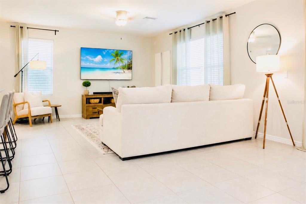 A bright living room features a white sofa, a wall-mounted television, and tile flooring — 17015 OVAL RUM DRIVE, WIMAUMA, FL