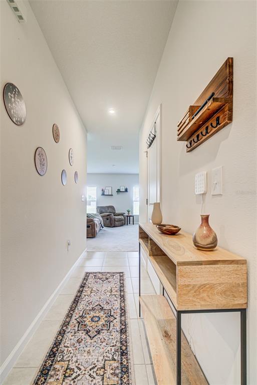 A hallway features a runner rug, a console table, wall decor, and a view into a living room — 1104 CATSKILL DRIVE, HAINES CITY, FL