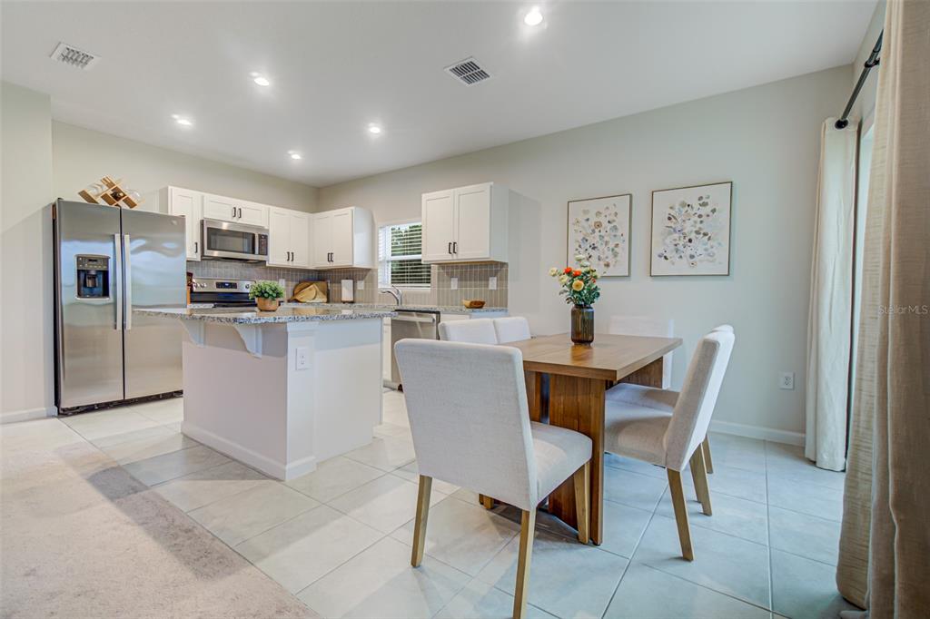 A kitchen with white cabinets, stainless steel appliances, and an adjacent dining area with chairs — 1104 CATSKILL DRIVE, HAINES CITY, FL