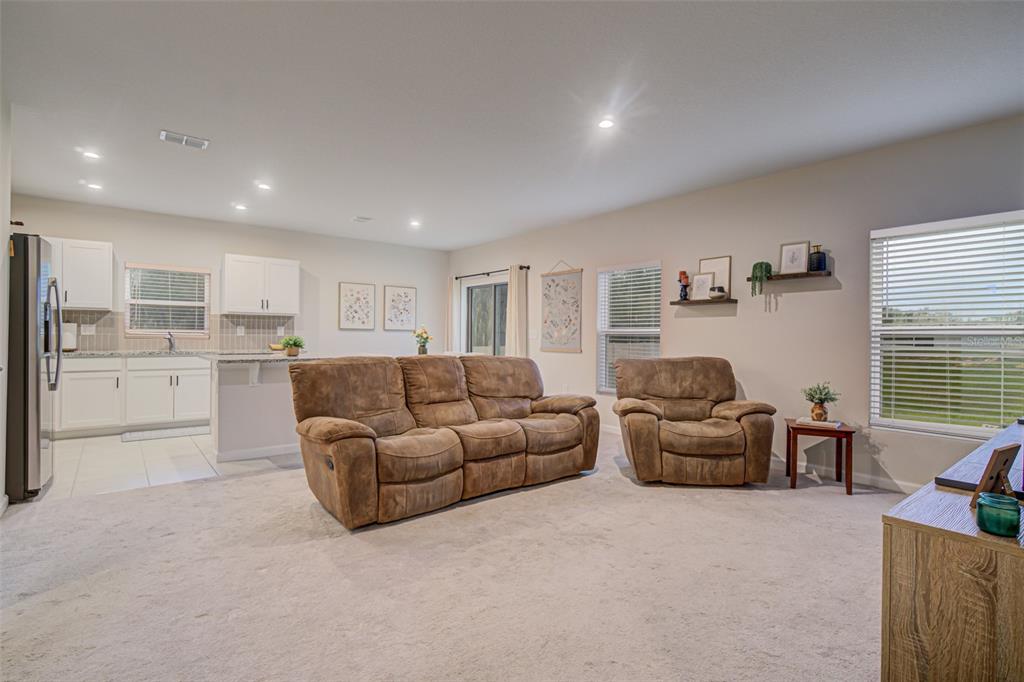A living room with carpeted floors and brown furniture opens to a white kitchen — 1104 CATSKILL DRIVE, HAINES CITY, FL