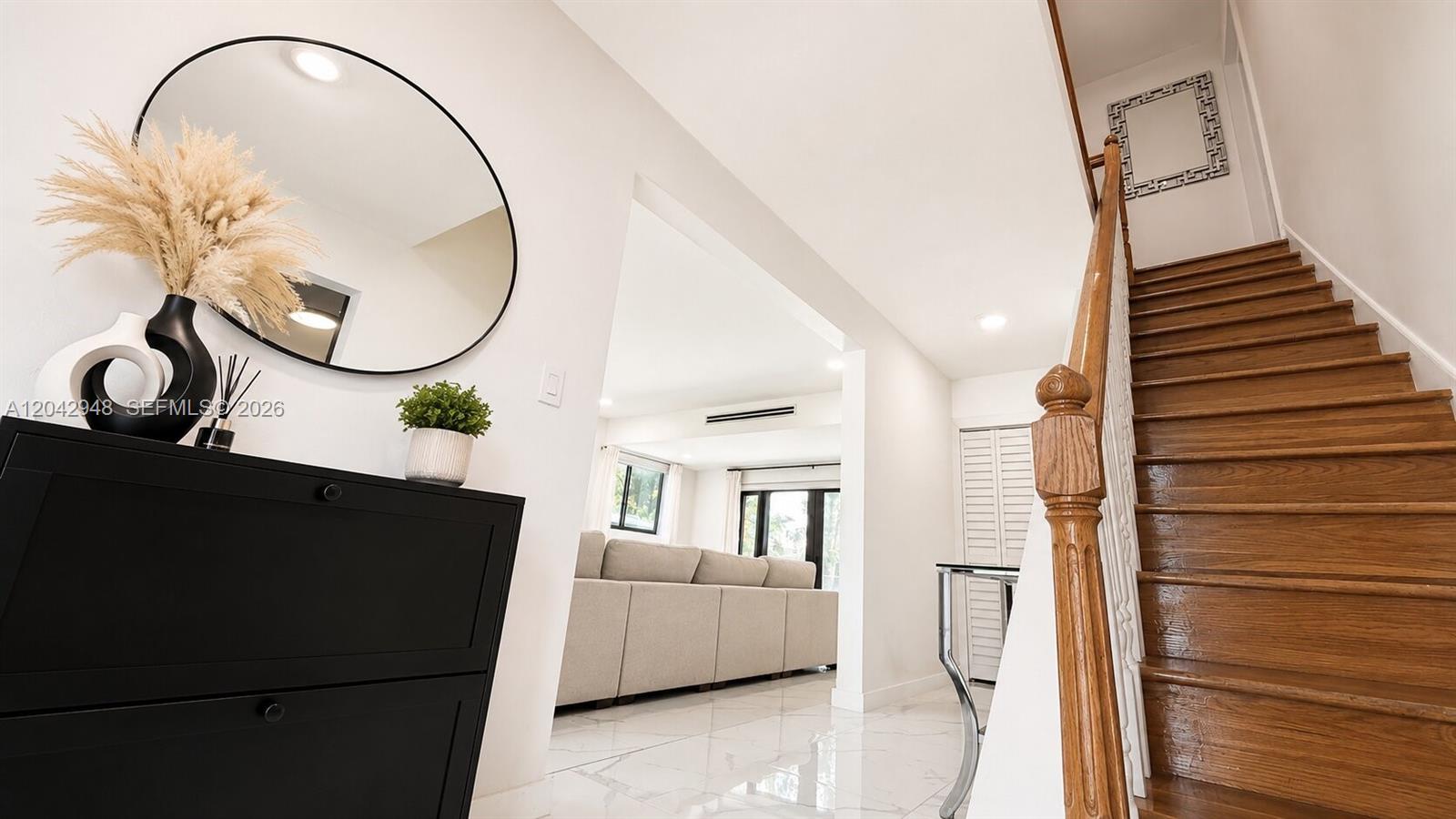 A foyer features a black cabinet, a round mirror, and a wooden staircase — 17790 SW 110th Ct, Miami FL 33157, MIAMI, FL