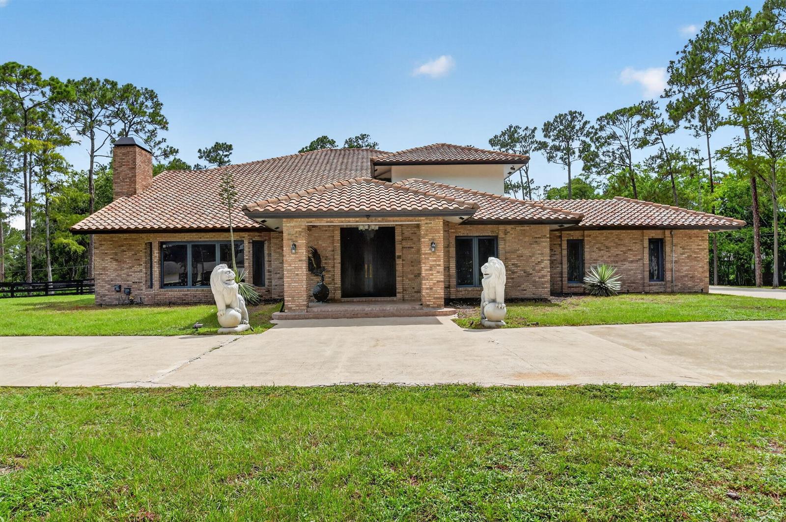 A single-story brick house with a tile roof features two lion statues flanking the entrance — 14780 Draft Horse Lane, Wellington FL 33414, WELLINGTON, FL
