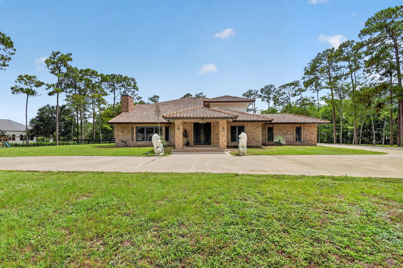 A single-story brick house with a tiled roof sits behind two lion statues — 14780 Draft Horse Lane, Wellington FL 33414, WELLINGTON, FL