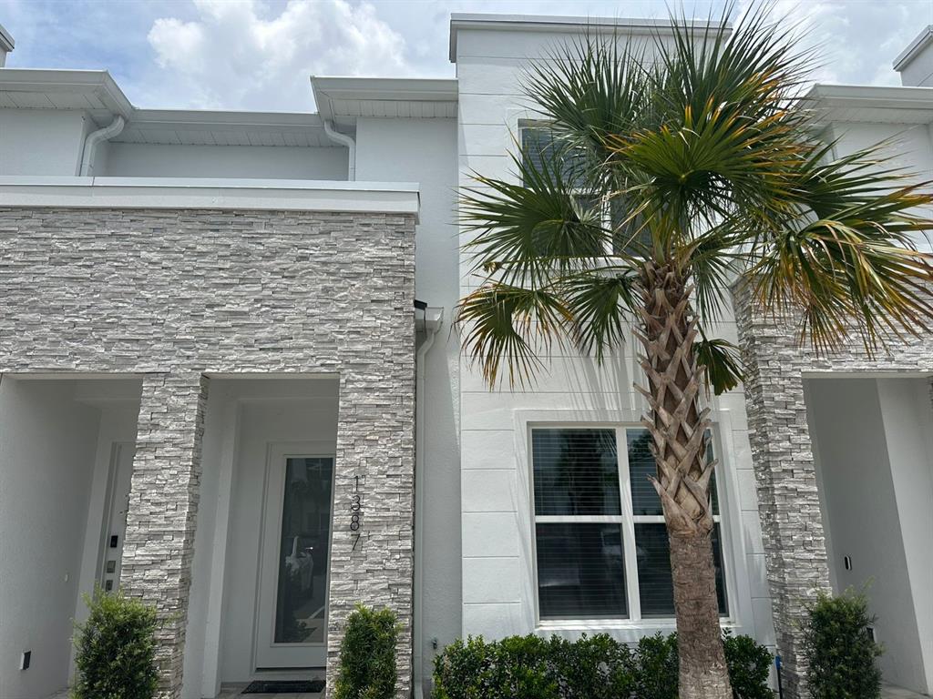 A two-story townhouse exterior features white stucco walls, stone veneer accents, and a palm tree — 1387 PEACEFUL NATURE WAY, CLERMONT, FL