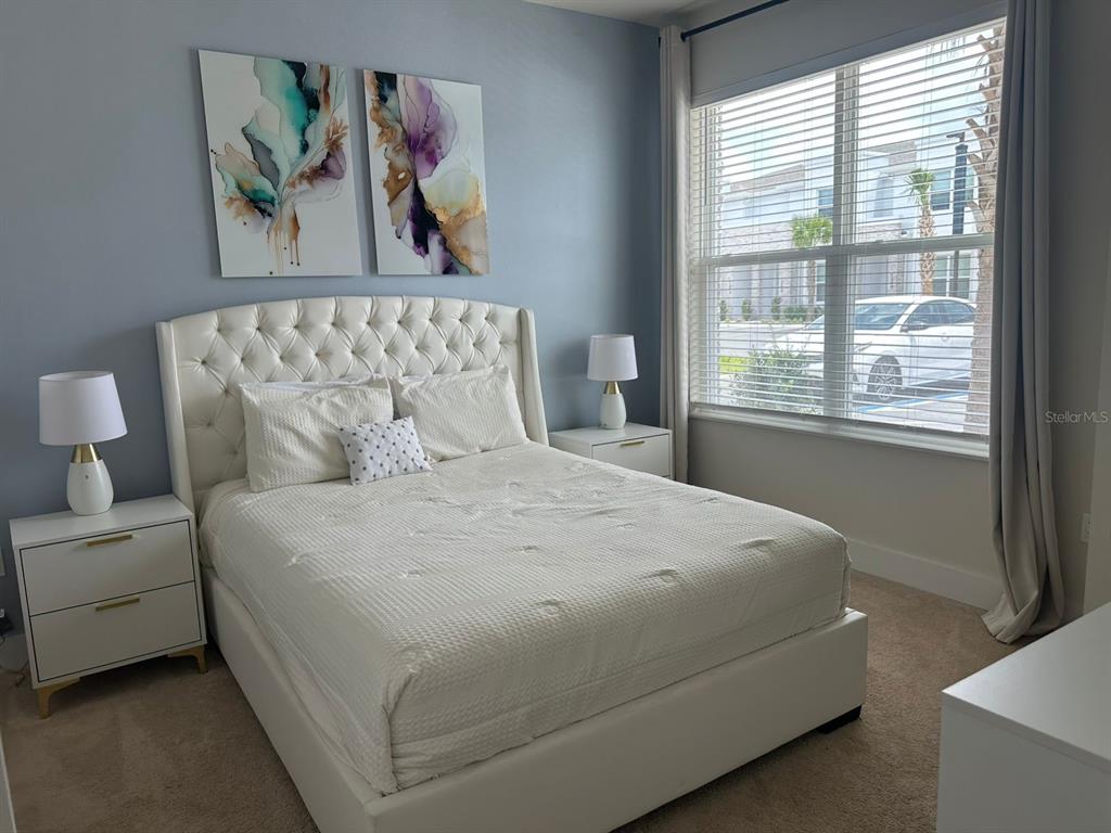 A bedroom features a white tufted bed, two nightstands with lamps, and abstract wall art — 1387 PEACEFUL NATURE WAY, CLERMONT, FL