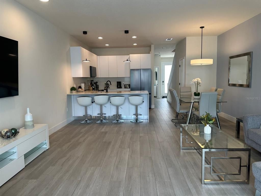 An open-concept living area features a modern kitchen with white cabinetry, bar seating, and dining — 1387 PEACEFUL NATURE WAY, CLERMONT, FL