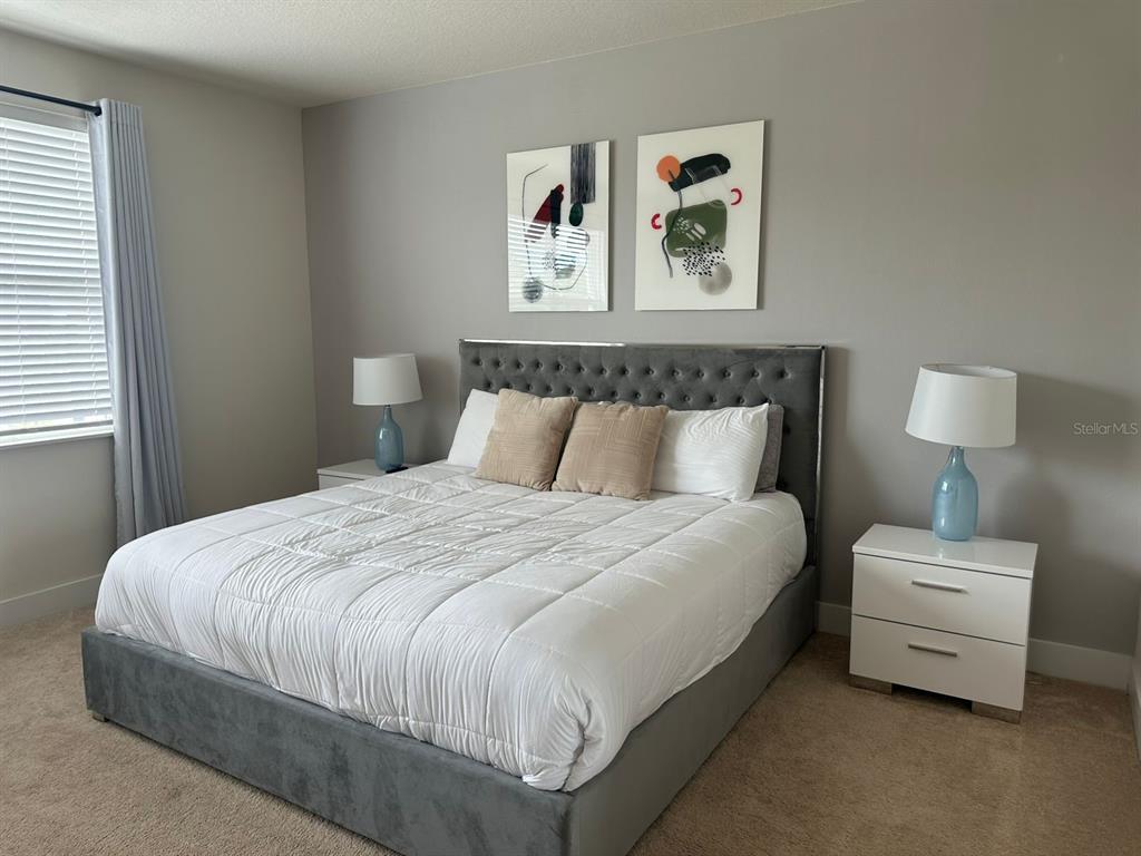 A bedroom features a tufted gray bed, two white nightstands, and two abstract wall paintings — 1387 PEACEFUL NATURE WAY, CLERMONT, FL
