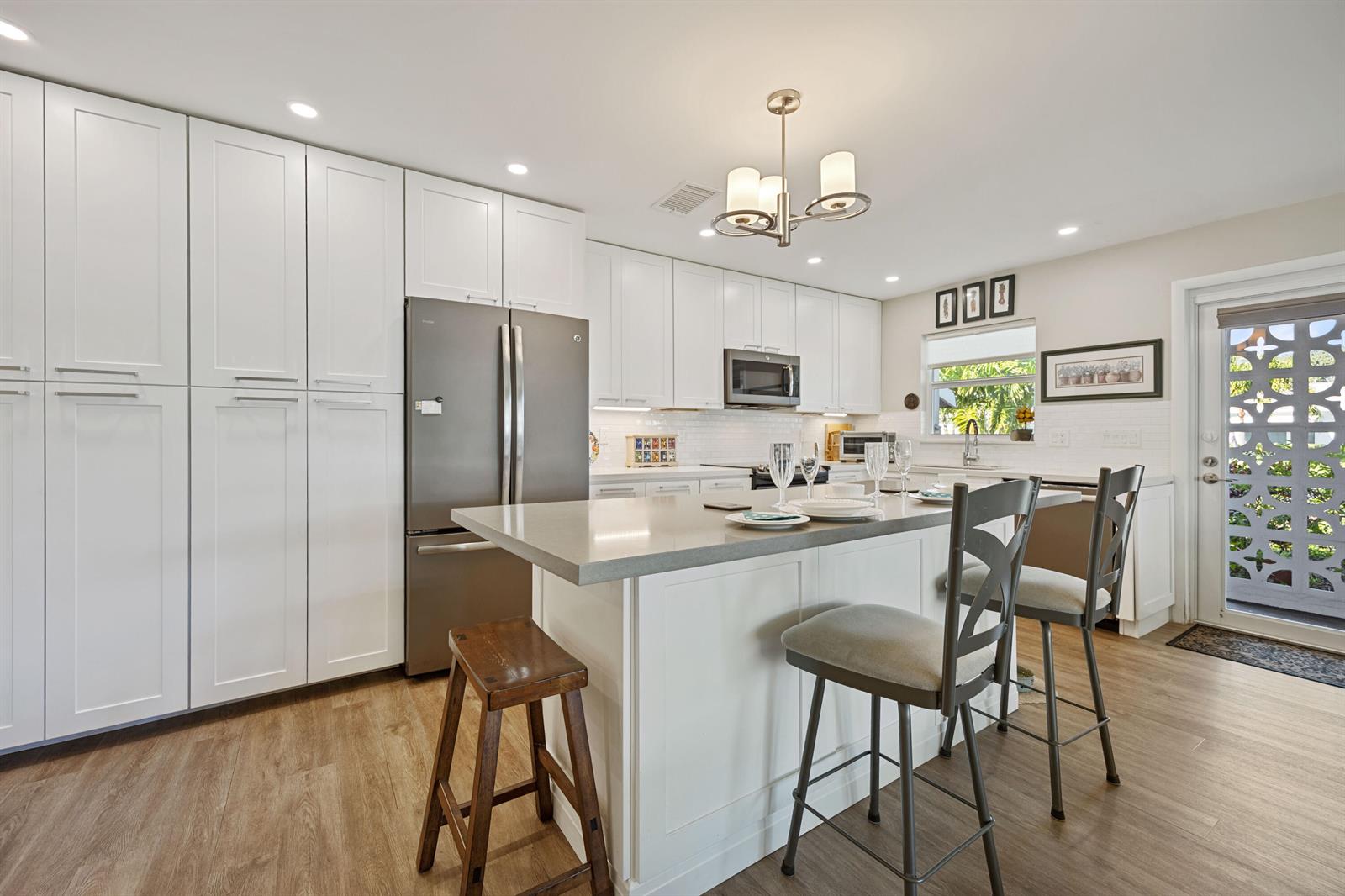A modern kitchen features white cabinetry, a gray island with seating, and a glass-paneled door — 200 South Boulevard # A, Boynton Beach FL 33435, BOYNTON BEACH, FL