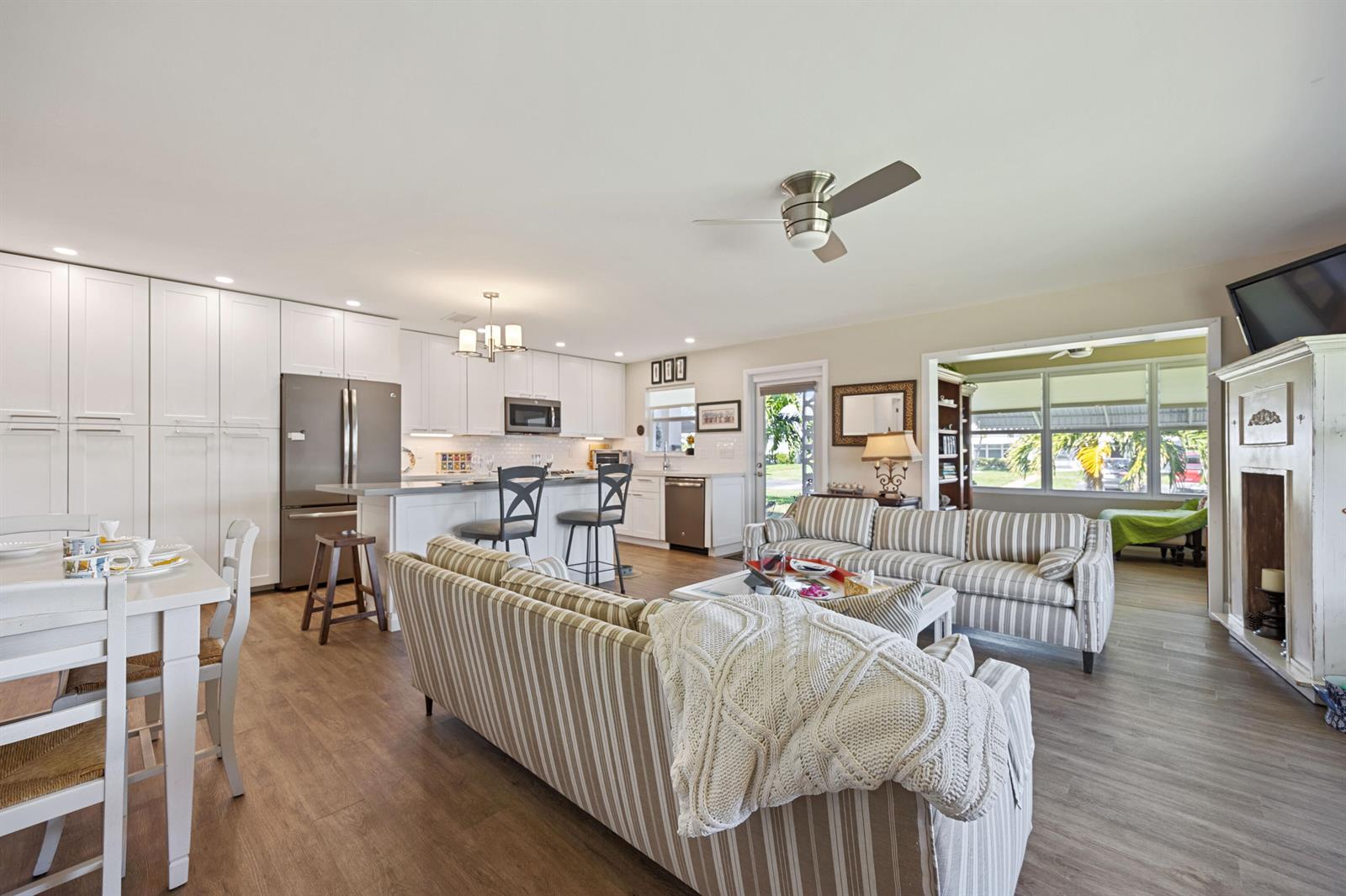 An open-concept living room and kitchen featuring striped sofas, white cabinetry, and wood-look flooring — 200 South Boulevard # A, Boynton Beach FL 33435, BOYNTON BEACH, FL