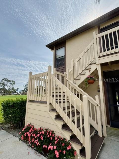 An exterior view shows a beige building with a wooden staircase leading to an upper balcony — 5753 AVISTA DRIVE, SARASOTA, FL
