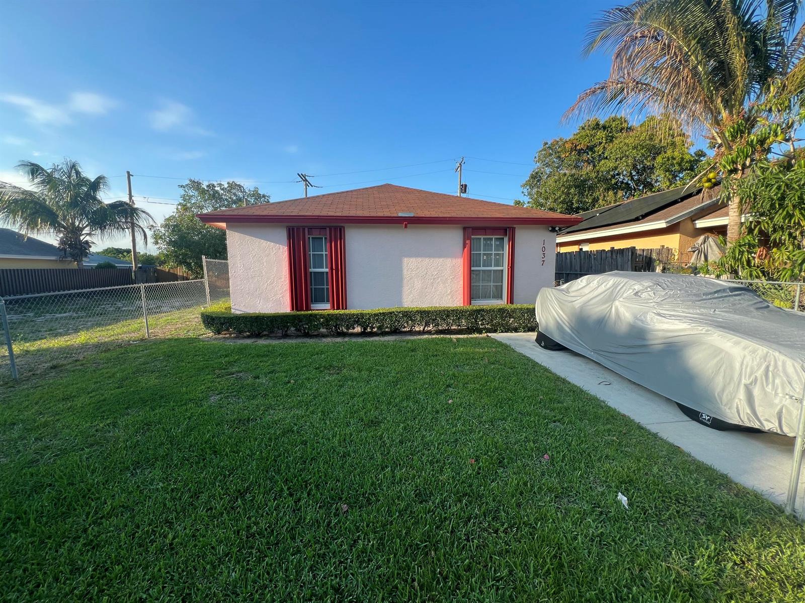A single-story house with a light-colored facade, red trim, and a covered car in front — 1037 17th Street, West Palm Beach FL 33407, WEST PALM BEACH, FL
