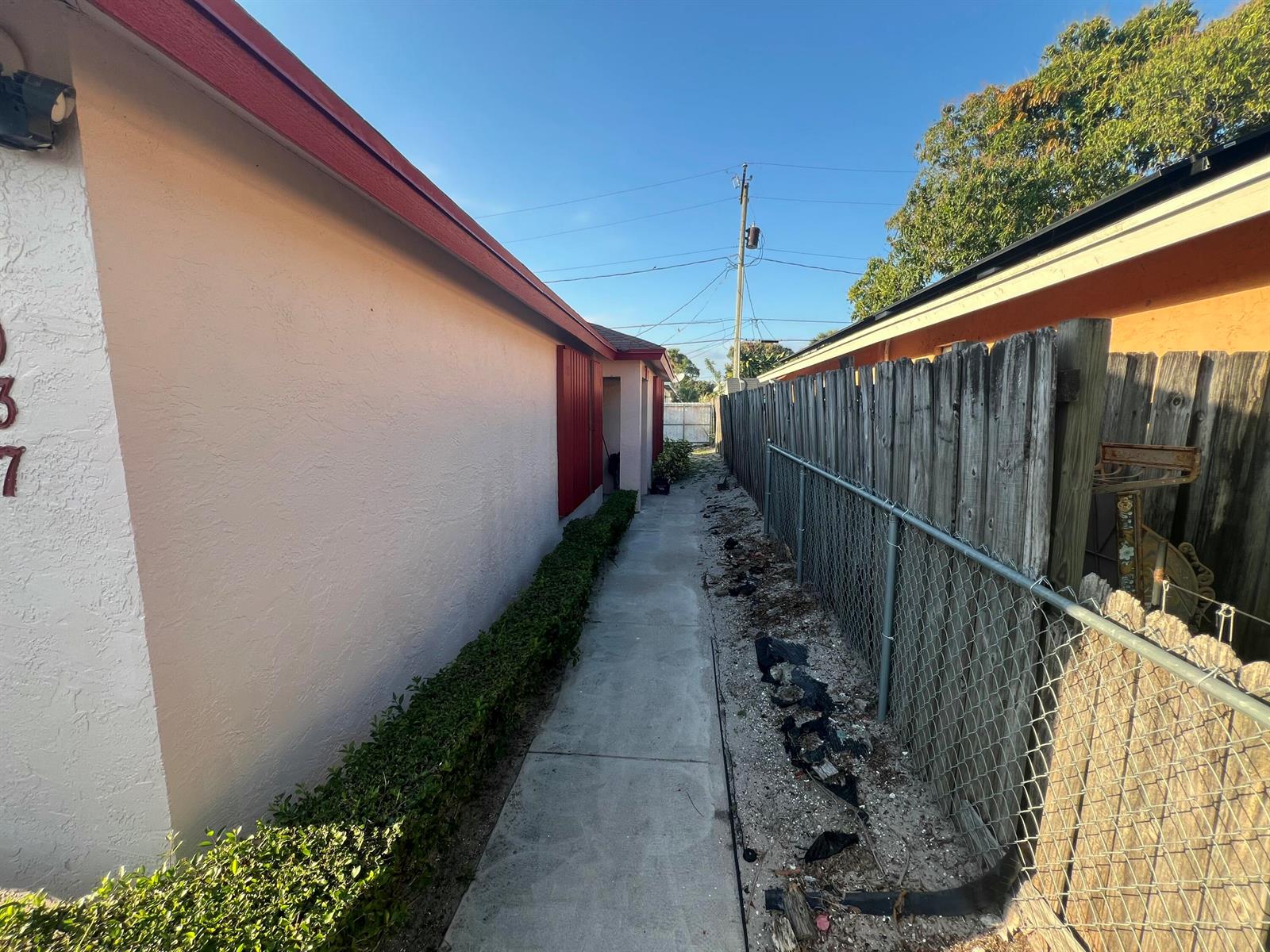 A narrow concrete walkway runs between a peach-colored house and a wooden fence — 1037 17th Street, West Palm Beach FL 33407, WEST PALM BEACH, FL