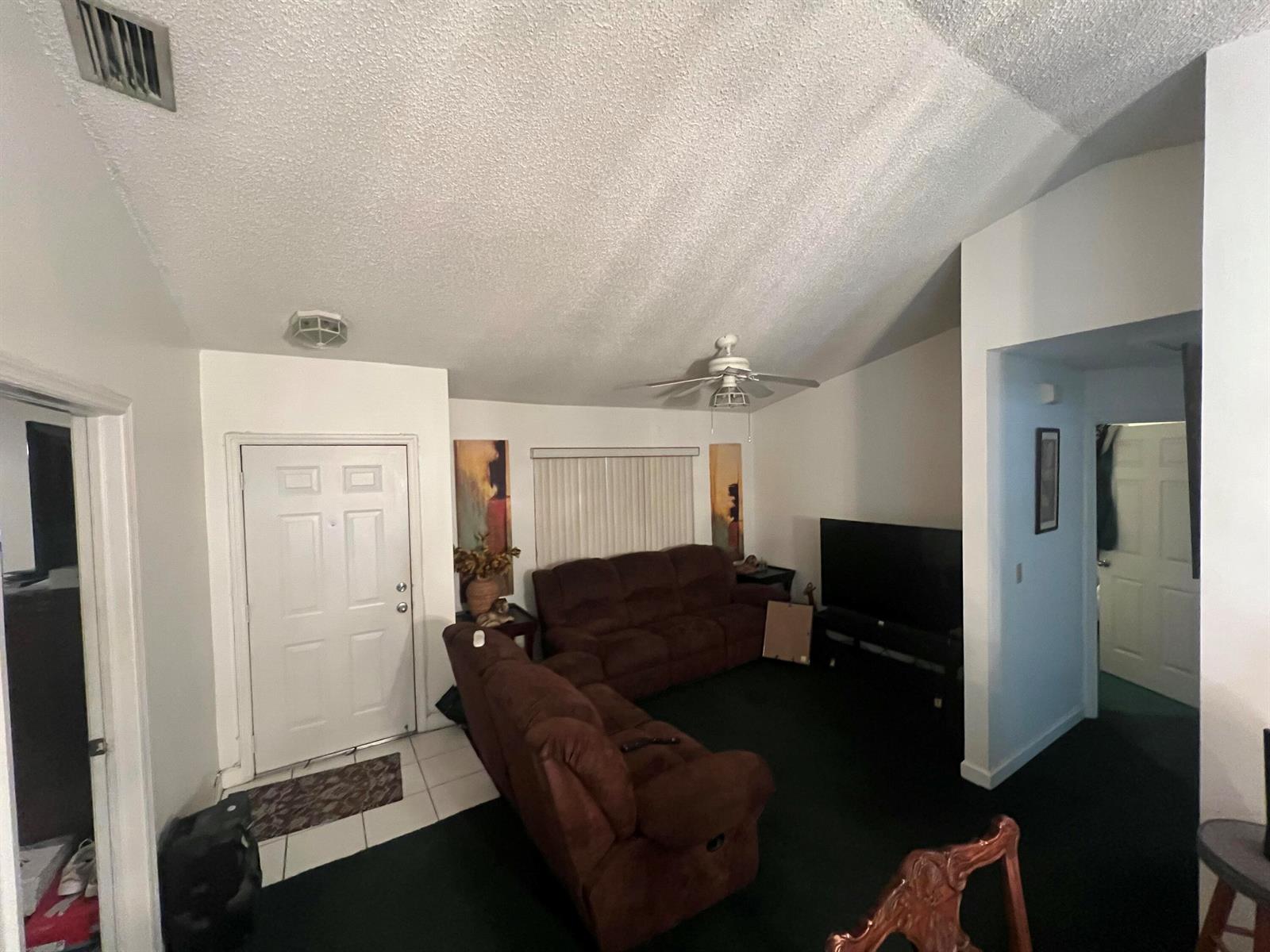 A living room features dark carpet, brown furniture, a vaulted ceiling, and a front door — 1037 17th Street, West Palm Beach FL 33407, WEST PALM BEACH, FL