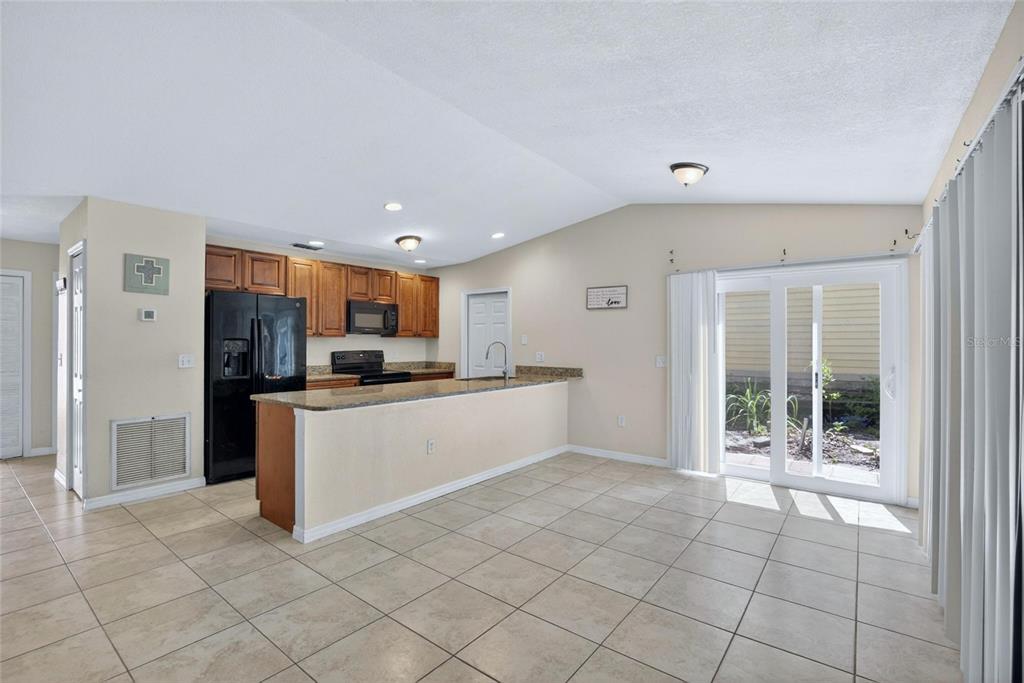 A kitchen with wood cabinets, black appliances, and a breakfast bar overlooks a tiled dining area — 7606 LEON AVENUE, TAMPA, FL