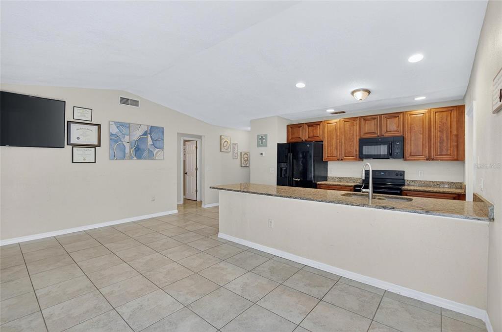 A kitchen with wood cabinets and granite countertops overlooks an open-concept tiled living area — 7606 LEON AVENUE, TAMPA, FL