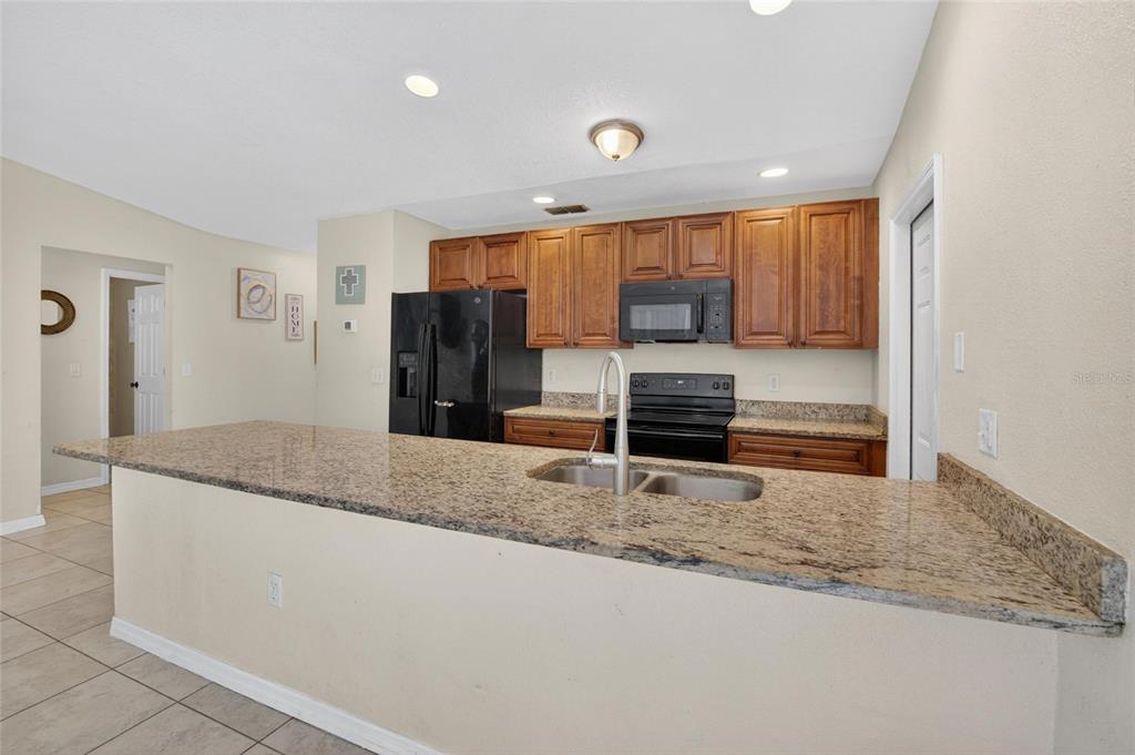 A kitchen features wood cabinets, granite countertops, a black refrigerator, and a breakfast bar island — 7606 LEON AVENUE, TAMPA, FL