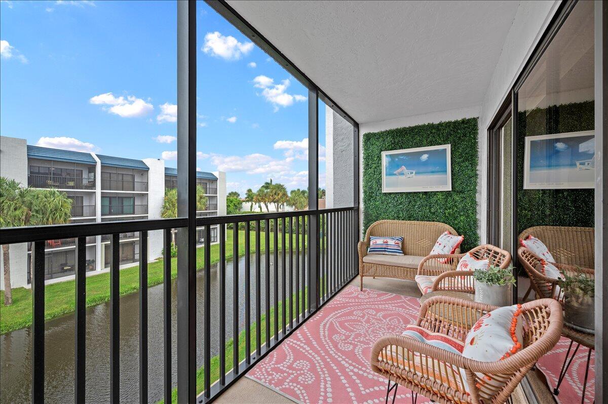 A screened-in balcony features wicker furniture, a pink patterned rug, and a green wall panel — 1605 S Us Highway 1 # A303, Jupiter FL 33477, JUPITER, FL
