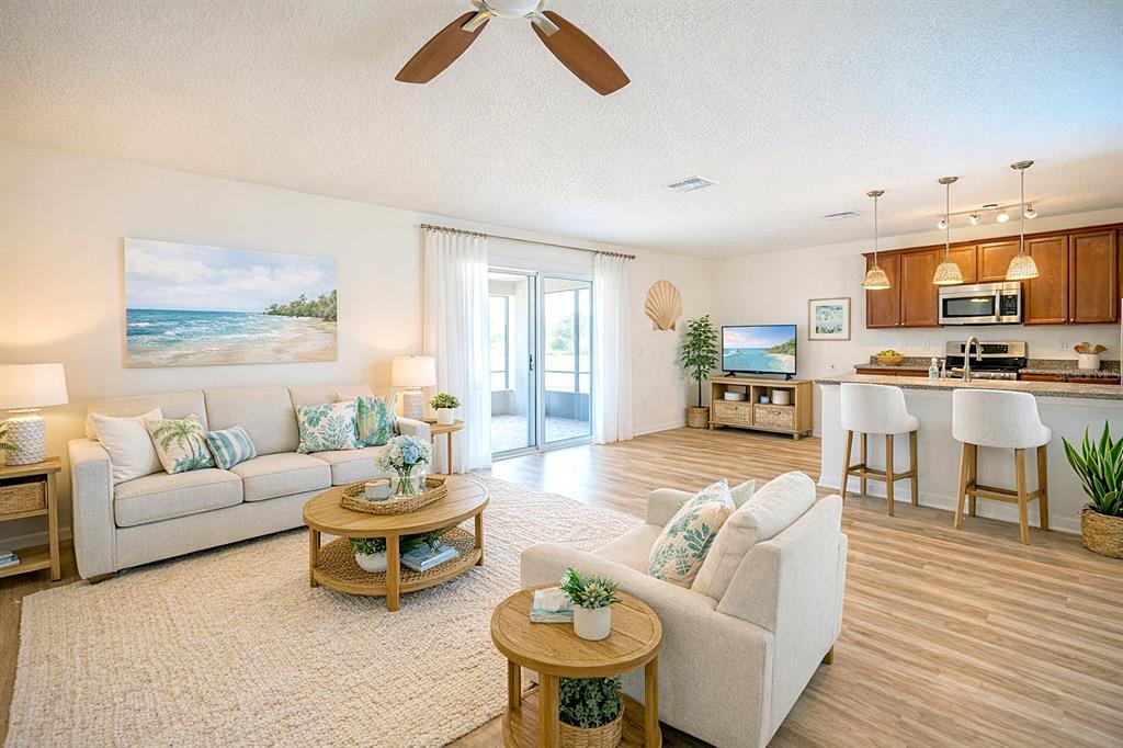 An open-concept living room and kitchen featuring light wood flooring, neutral furniture, and coastal decor — 436 GREAT FALLS LANE SW, PALM BAY, FL