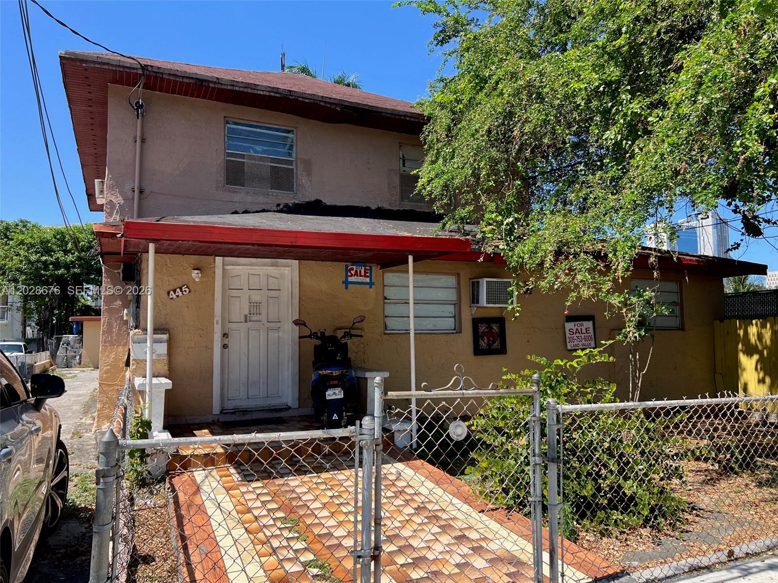 A two-story tan house with a red awning, a tiled front porch, and a chain-link fence — MIAMI, FL