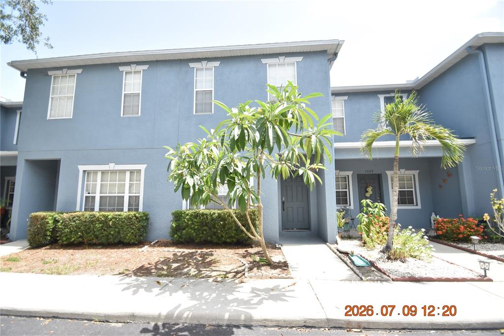A two-story blue townhouse exterior features a front walkway, landscaping, and a small palm tree — 13121 KINGS CROSSING DRIVE, GIBSONTON, FL