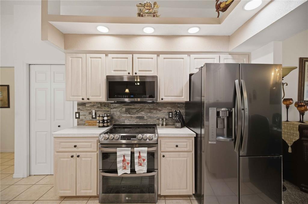 A kitchen features light wood cabinets, stainless steel appliances, and a stone tile backsplash — 4710 W MUSTANG BOULEVARD, BEVERLY HILLS, FL