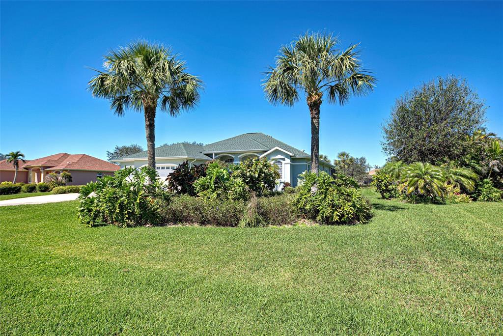 A single-story house with a green roof is surrounded by palm trees and landscaping — 1078 BOUNDARY BOULEVARD, ROTONDA WEST, FL