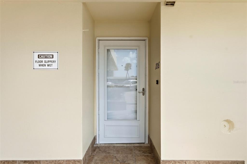 A white storm door with a glass panel is centered on a beige exterior wall — 4775 COVE CIRCLE UNIT 106, ST PETERSBURG, FL