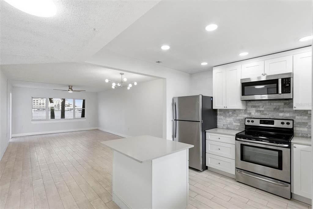 A kitchen with white cabinets and stainless steel appliances opens into a bright living area — 4775 COVE CIRCLE UNIT 106, ST PETERSBURG, FL