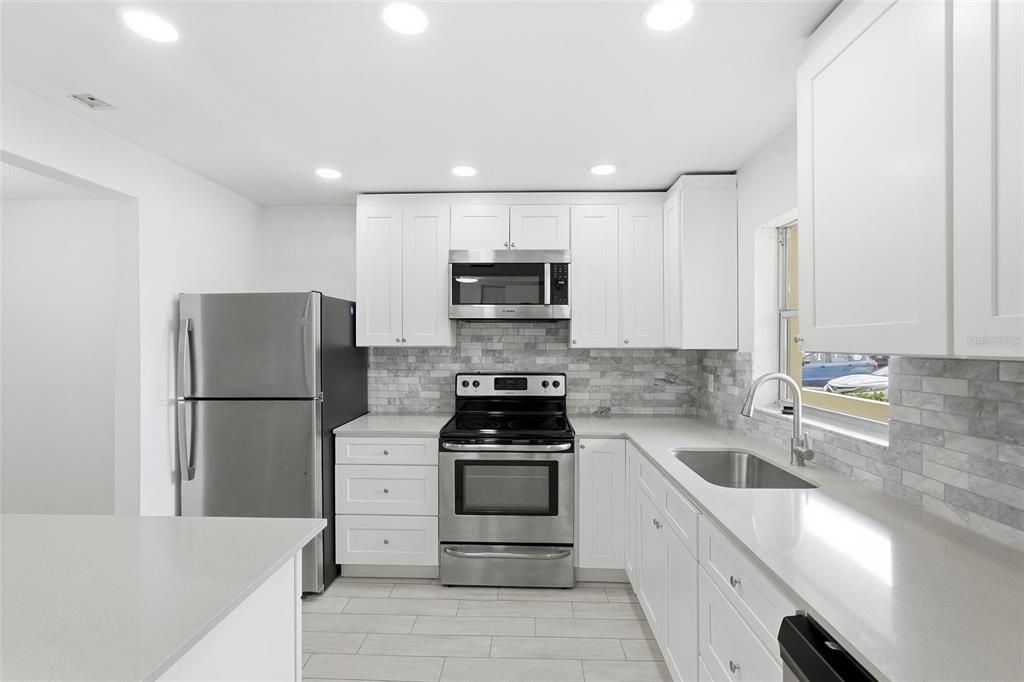 A modern kitchen features white cabinets, stainless steel appliances, and a gray tile backsplash — 4775 COVE CIRCLE UNIT 106, ST PETERSBURG, FL