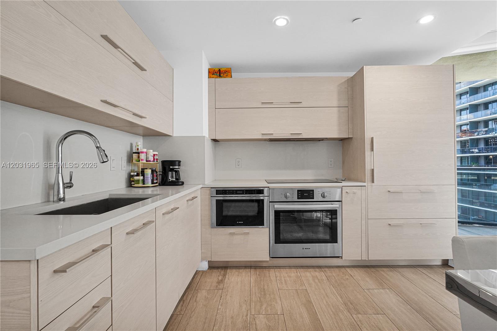 A modern kitchen features light wood cabinetry, stainless steel appliances, and a view of balconies — 45 SW 9th St # 2901, Miami FL 33130, MIAMI, FL