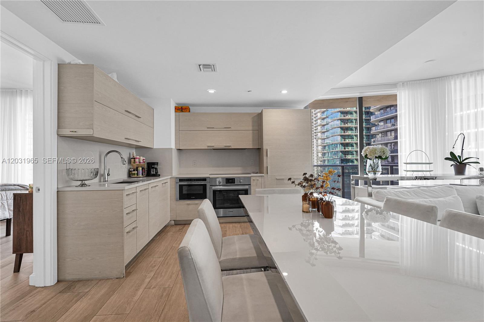 A modern kitchen features light wood cabinetry, white countertops, and a dining table with chairs — 45 SW 9th St # 2901, Miami FL 33130, MIAMI, FL
